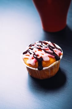 cupcake with pink frosting and red cup on a wooden background