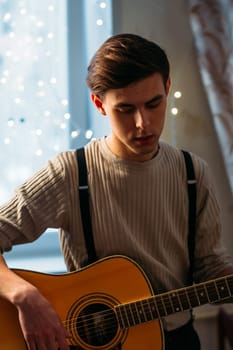 Young man sitting at home and playing guitar dramatic