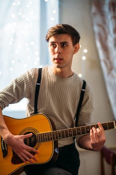 Young man sitting at home and playing guitar dramatic