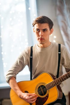 Young man sitting at home and playing guitar dramatic