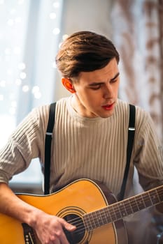 Young man sitting at home and playing guitar dramatic