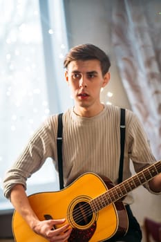 Young man sitting at home and playing guitar dramatic