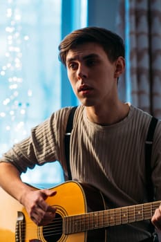 Young man sitting at home and playing guitar dramatic