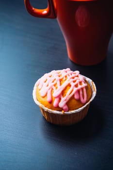 cupcake with pink frosting and red cup on a wooden background