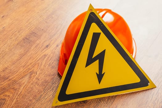 Safety sign high voltage and red hard hat on a wooden background