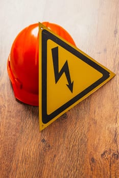 Safety sign high voltage and red hard hat on a wooden background
