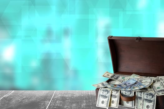 Finance concept. Wooden box full with US 100 dollars on table with abstract blurred bank houses silhouette background.  Concept of money and earnings. Space.