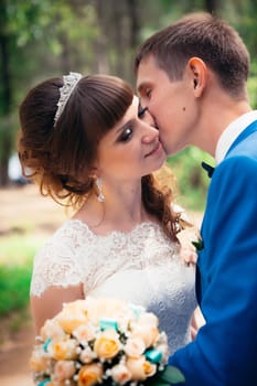 young bride and groom kissing on the background of the forest and the road.