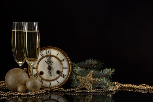 Two wineglasses with champange, bottle, gift box, clock and christmas ornament on a black background with reflection. Copy space. Christmas and New Year background