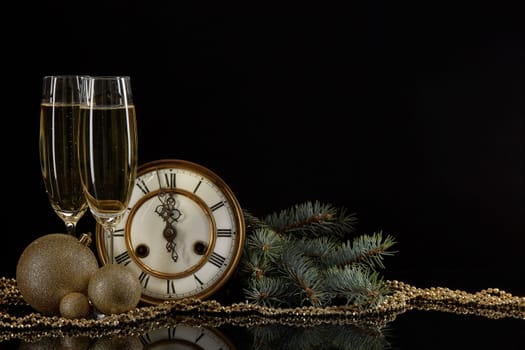 Two wineglasses with champange, fir tree branches, clock and christmas ornament on a black background with reflection. Copy space. Christmas and New Year background