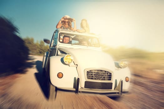 Group of happy friends in a car at sunset in summer.
