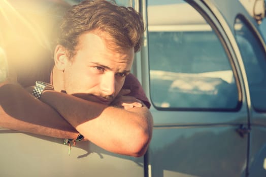 Handsome young man looking over a car window at sunset