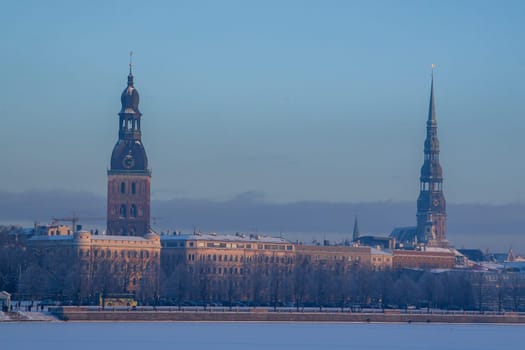 Riga view in winter. Riga, capital city of Latvia in winter time. View of St Peter's Church and St. Jacob's Cathedral. View of Old Riga with frozen river Daugava in the foreground. City Riga with background of blue sky.