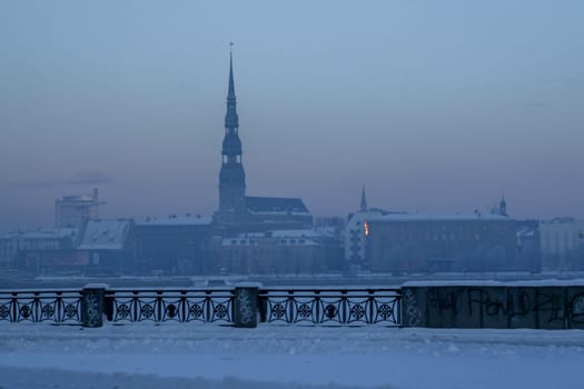 Riga view in winter  Riga, capital city of Latvia in winter time. View of St Peter's Church in winter. View of Old Riga with frozen river Daugava in the foreground. City Riga with background of blue sky.