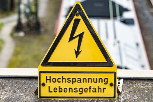 Close-up of a yellow high voltage caution sign mounted on a wall