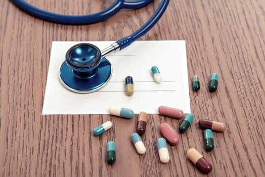 prescription with colorful pills and stethoscope on wooden ground