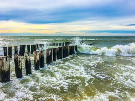 big waves collapsing against wooden poles in a sea ocean beach landscape