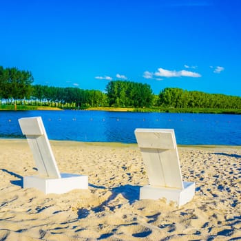 two white beach chairs at a sand beach lake landscape