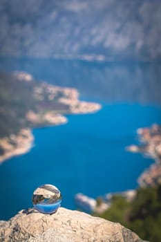 Stunning landscape of the Bay of Kotor and Lovcen National Park in Montenegro reflected in a large glass ball placed on a large boulder