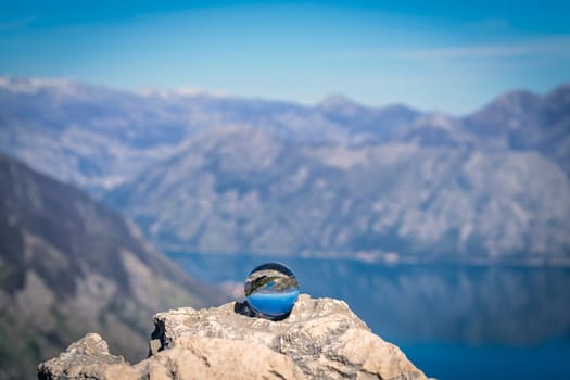 Stunning landscape of the Bay of Kotor and Lovcen National Park in Montenegro reflected in a large glass ball placed on a large boulder