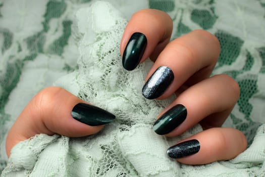 Female hand with dark green nails is holding bright green lace, manicure concept.