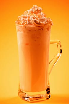 The orange frothy drink with whipped cream is on yellow background. Smoothie or milkshake.