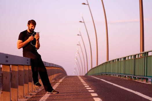 The man is using phone for morning recreation at the bridge outdoors.