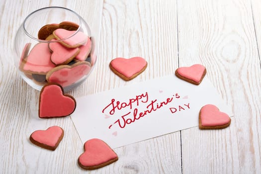 Cookies in the form of heart and greeting card lying on a light wooden background. Valentine's Day card