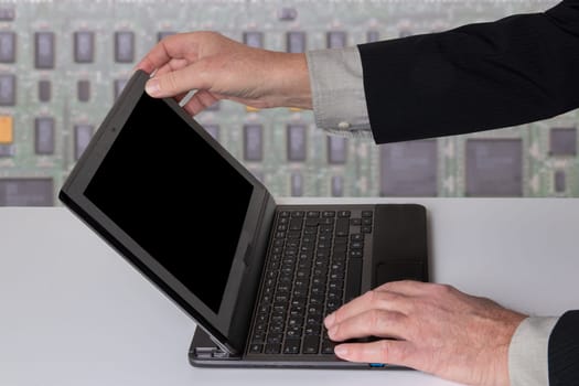 Hands of a unrecognizeable businessman working with a modern portable computer on a white table. Computer in front of abstract bright technology background.