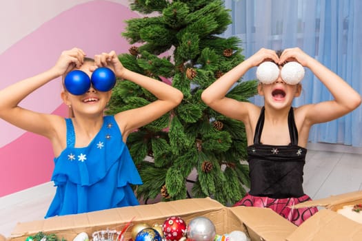 Two girls put big Christmas balls to their eyes