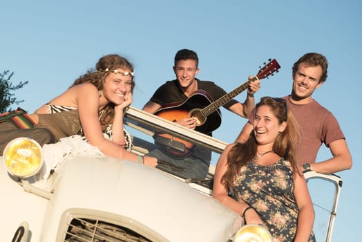 Group of happy people in a car at sunset in summer.
