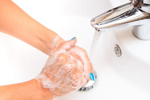 Female hands under running water in the sink