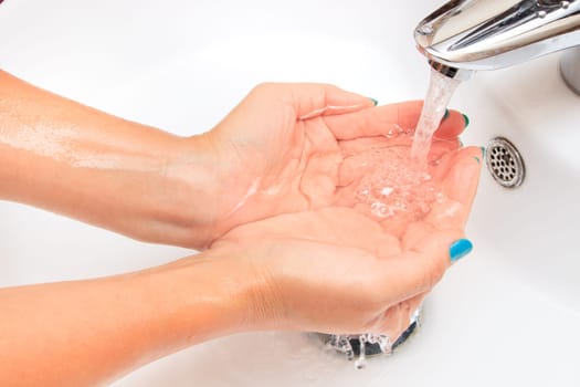 Female hands under running water in the sink
