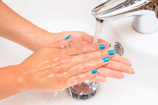 Female hands under running water in the sink