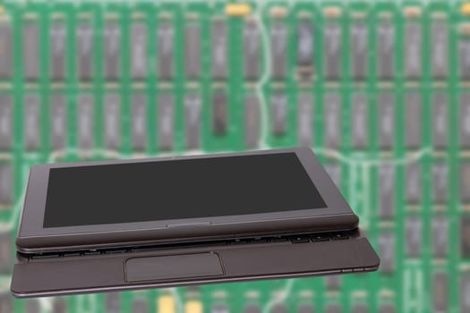 Computer technology background. Close up of modern portable laptop with a dark or black blank screen in front of bright blurred green digital electronic circuit board. PCB. Space.