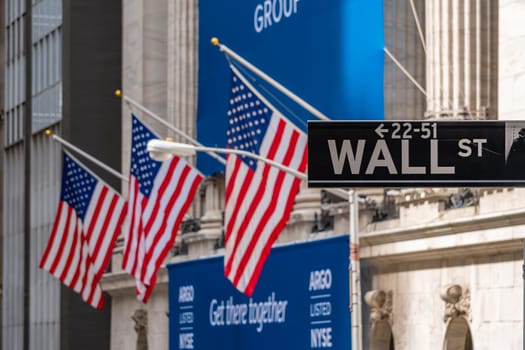 New York, USA - May 8, 2018: Wall Street sign near New York Stock Exchange with flags of the United States. It is the world's most significant financial center.