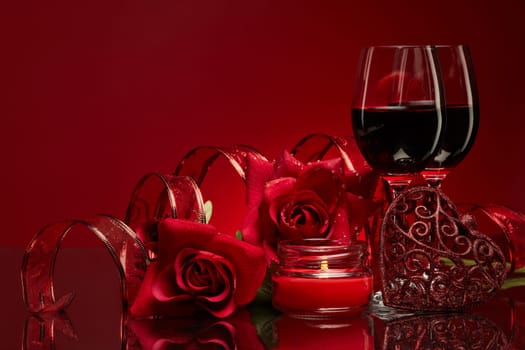 Still life with roses, red hearts and two glasses with wine on a red background. Valentine's Day card with copy space. Design element for romantic greeting card, wedding invitation