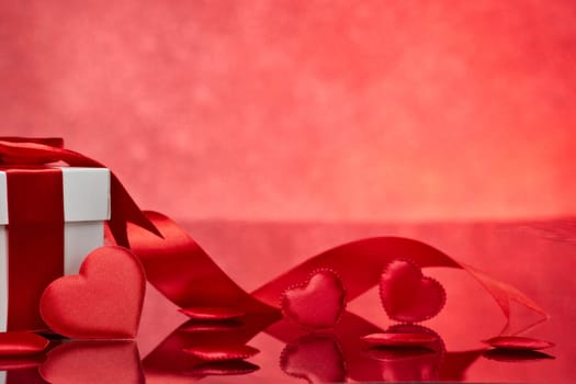 Gift box and red satin hearts on a red background. Valentine's Day card with copy space. Design element for romantic greeting card, wedding invitation, Women's Day postcard