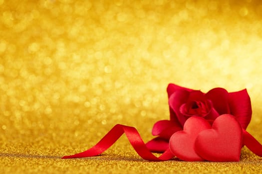 Two decorative hearts and red rose on a glittering gold background with copy space. Valentine's Day card. Design element for romantic greeting card, wedding invitation
