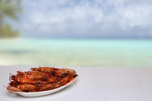 Table top on seafood background. Fresh grilled big prawn tiger or shrimps on a white table in front of abstract blurred tropical beach with blue sky. Template for your product display montage. Space for advertising.