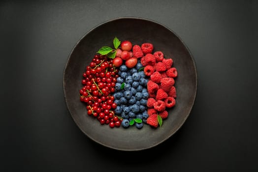 Mix of fresh berries in a bowl on black background