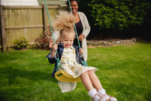 Little girl having fun while being pushed on a swing by her mother.
