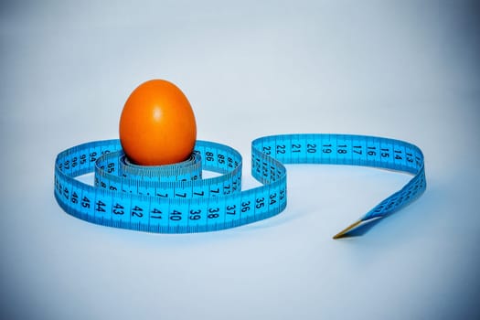 Egg wrapped in blue measuring tape, slimming concept.