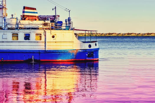 A cruise tourist ship is reflected in the water at dawn.