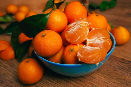 many fresh mandarin oranges in blue bowl, standing on a wooden table