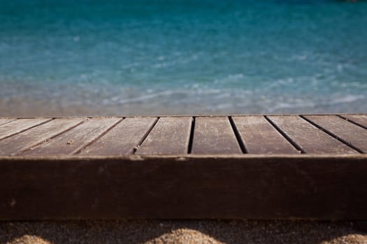 wooden plank in sand and blue sea in the background