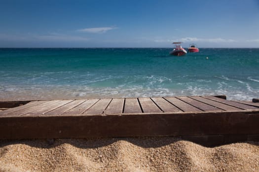 wooden plank in sand and blue sea in the background