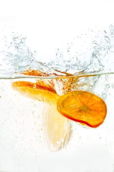 orange halves falling into water on white background.