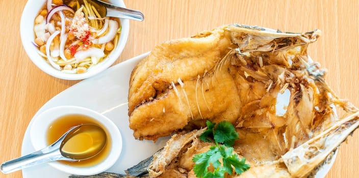 Deep fried seabass with sweet fish sauce eat with spice mango salad on wooden background, Thai groumet cuisine crop for website banner