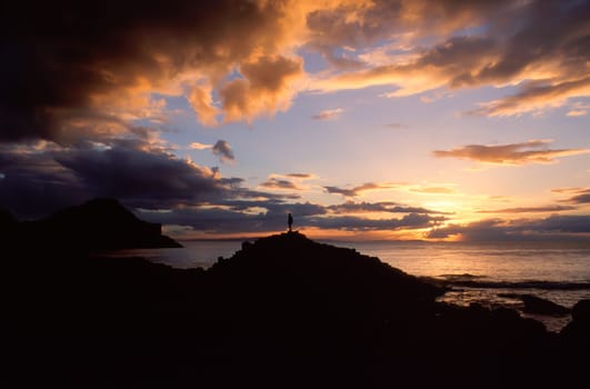 A lonely man standing on the rocks observes the beautiful sunset light on the ocean, a short break along the route of the Giant's Causeway, Northern Ireland